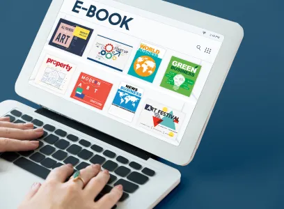 A person using a laptop with a screen displaying an e-book library interface, showcasing various book categories such as "art," "world," and "green businesses.